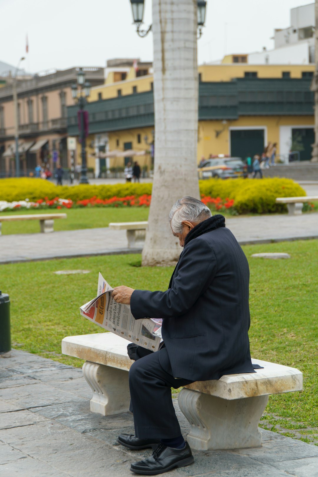 Senior man reading a newspaper and smiling on a park bench